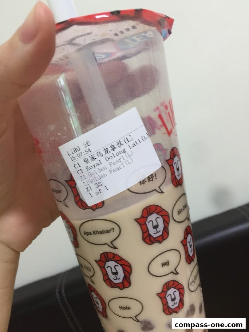 A hand holds a LiHO TEA cup with a sticker showing drink details and multilingual greetings.