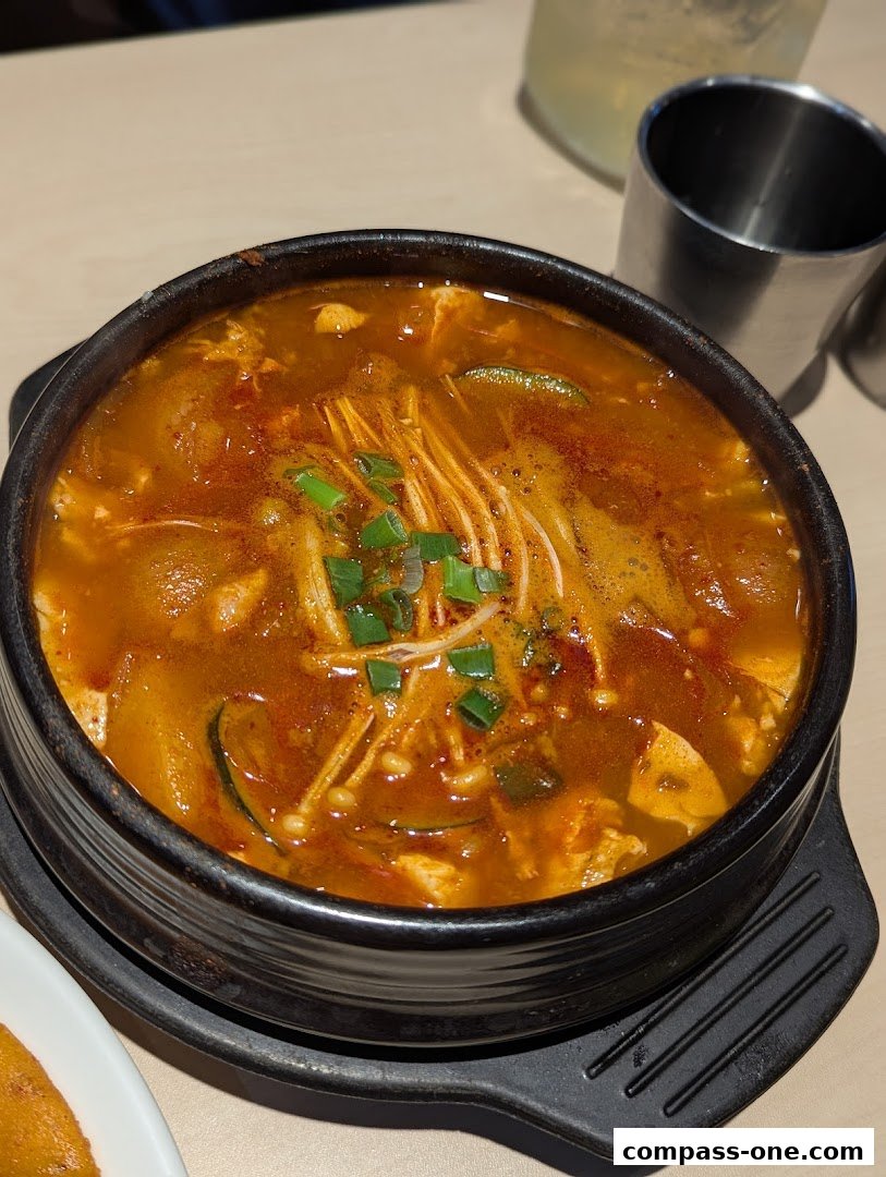 A steaming bowl of Korean soft tofu stew with enoki mushrooms and green onions.