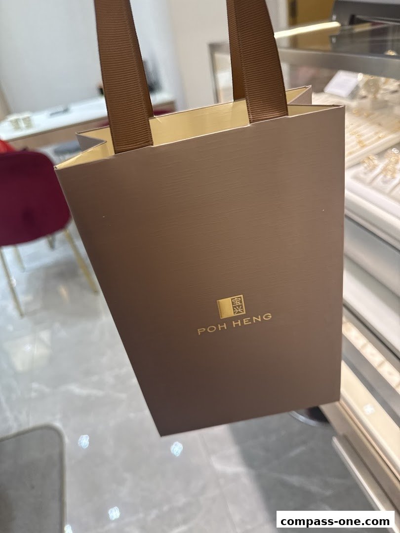 A brown shopping bag with the Poh Heng Jewellery logo is held up in front of a display case.