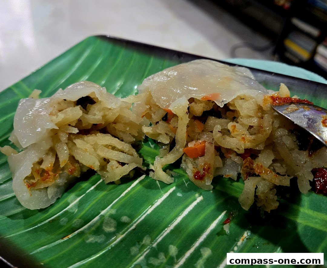 A close-up of a steamed dumpling filled with shredded vegetables and spices on a green banana leaf plate.