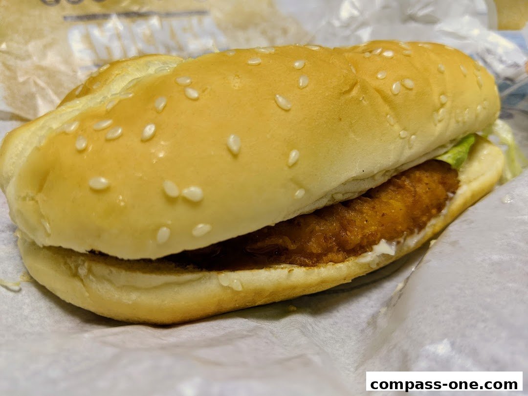 A close-up shot of a crispy chicken sandwich with lettuce and sauce on a sesame seed bun.