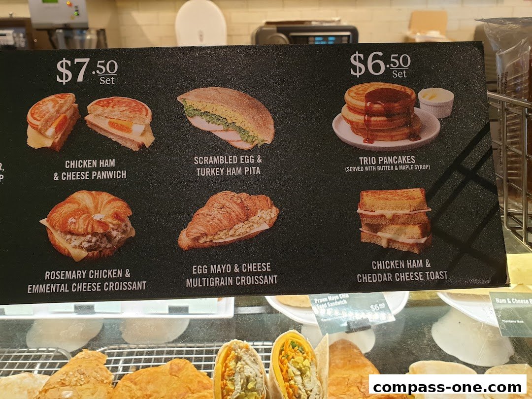 A menu board displaying various sandwiches, croissants, and pancakes with prices.