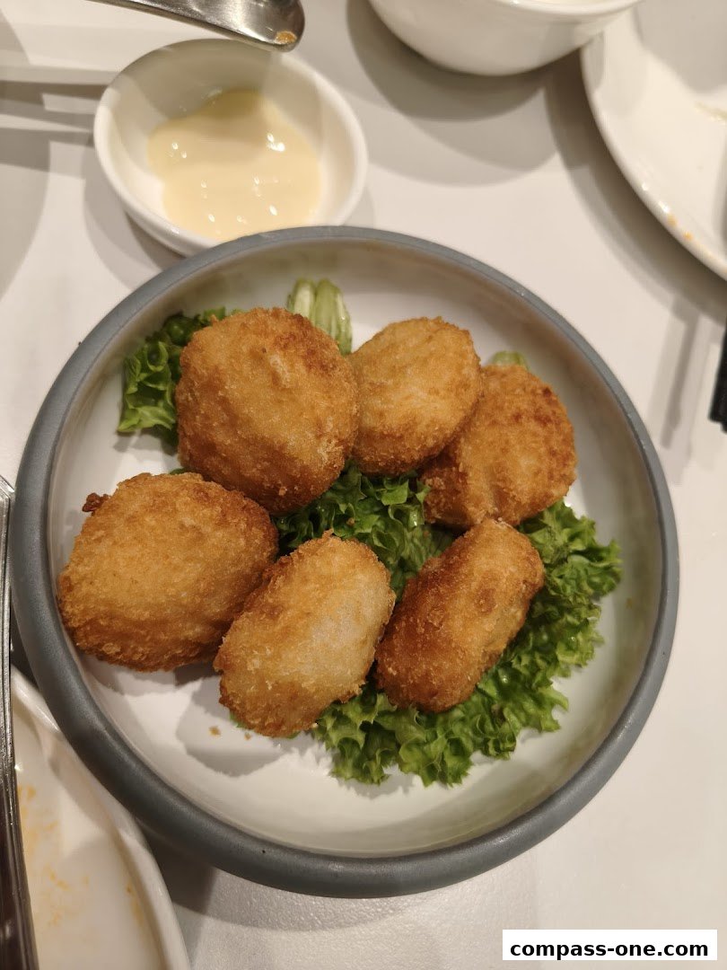 A bowl of golden-brown fried croquettes served on a bed of lettuce with a side of dipping sauce.