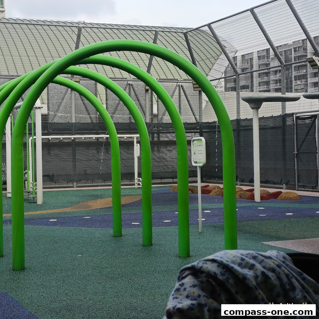 A colorful outdoor water play area with green arches and a soft ground surface.