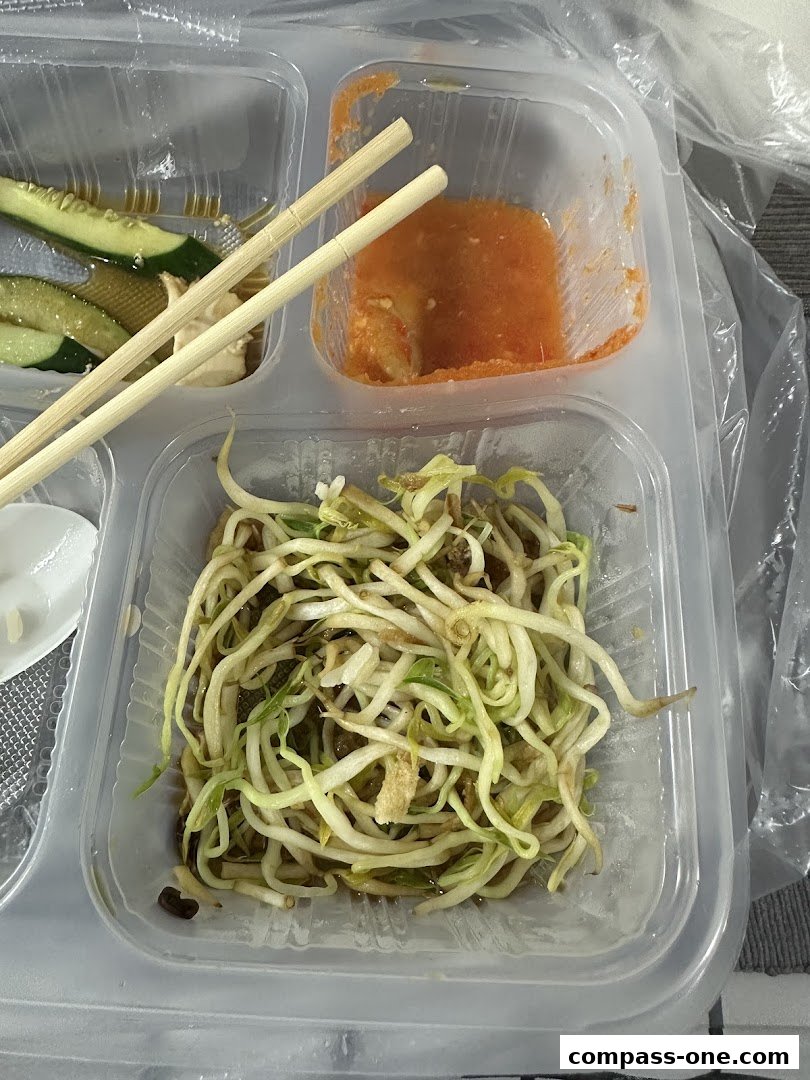 A close-up of a takeaway container with bean sprouts, cucumber slices, and dipping sauce.