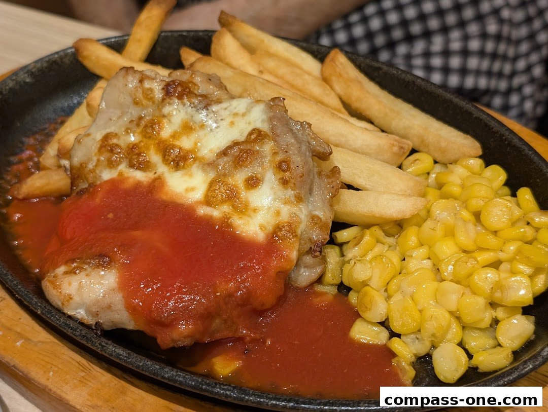 A sizzling plate of chicken with cheese, tomato sauce, fries, and corn.