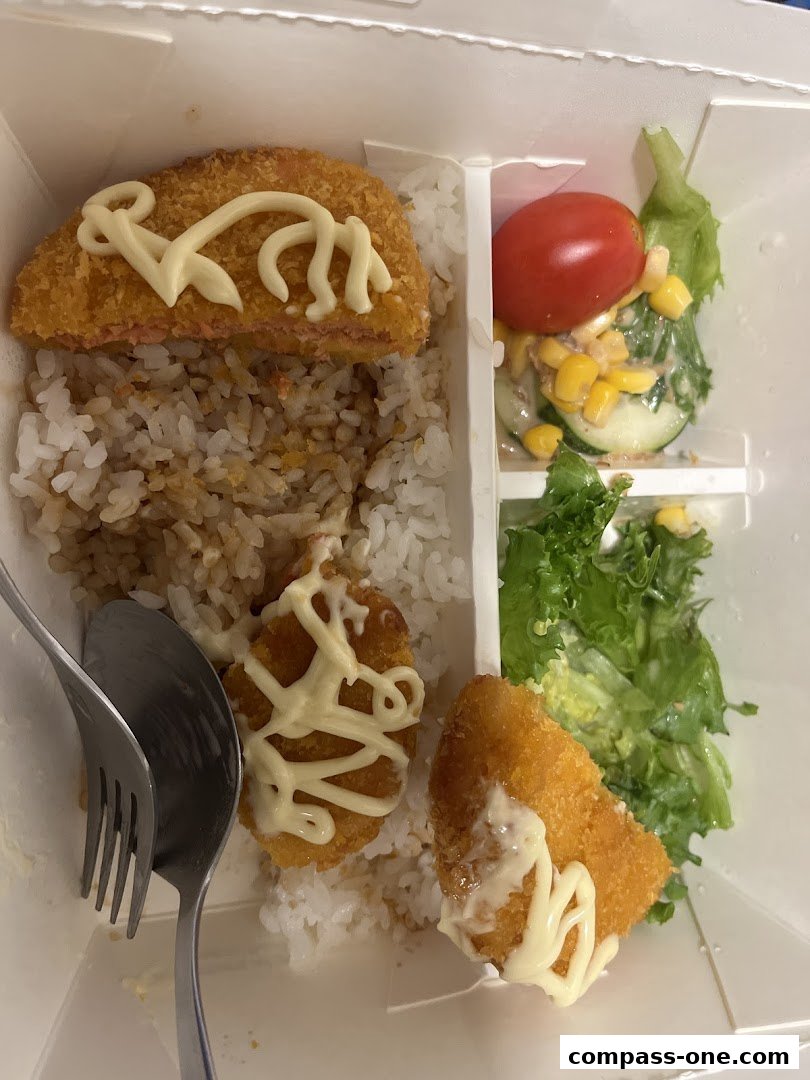 A bento box with rice, fried fish, and a side salad with tomato and corn.