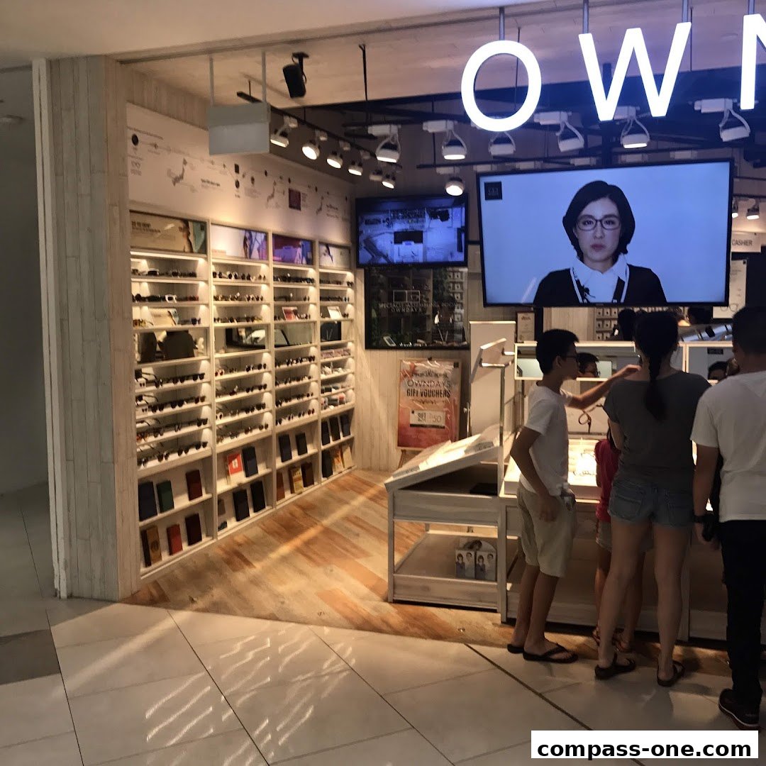 Interior of an OWNDAYS eyewear store with shelves of glasses and customers browsing.