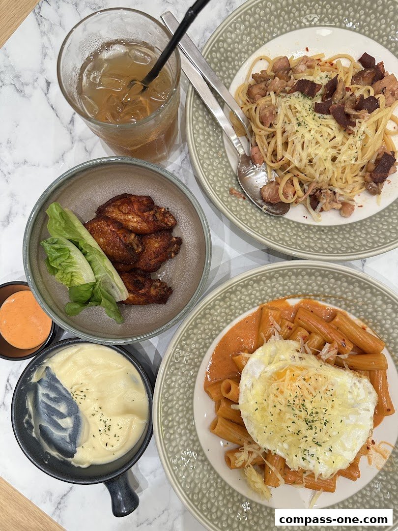 A table spread with Italian food including pasta, chicken wings, mashed potatoes, and a drink.