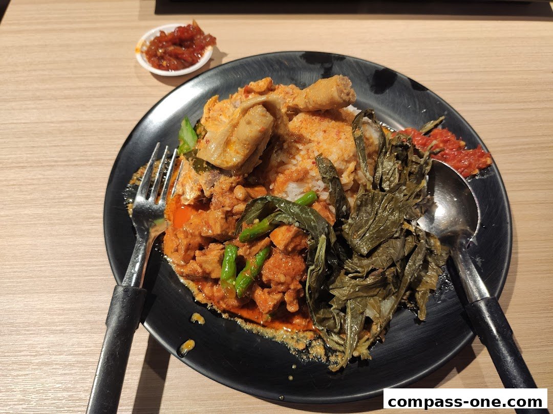 A plate of rice with chicken, vegetables, and sambal, served with a fork and spoon.