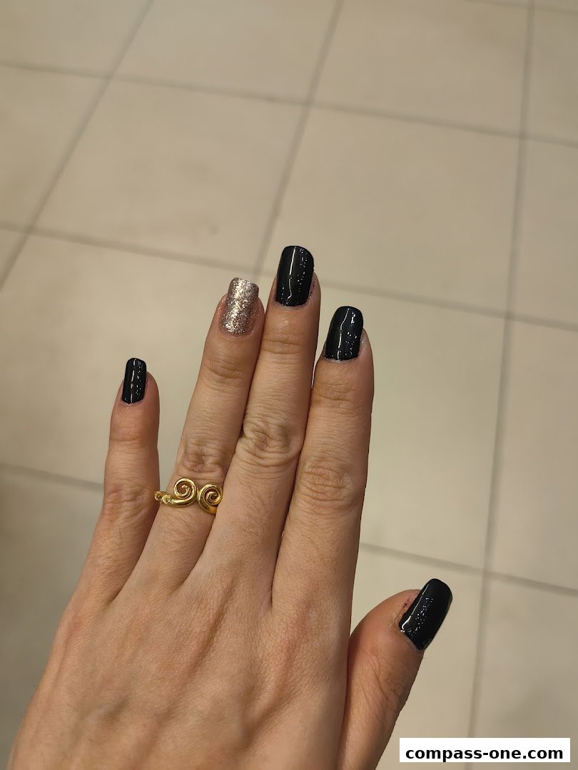 A hand with black and glittery nails and a gold ring.