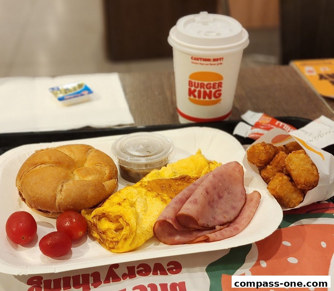 A Burger King breakfast meal with a bagel, omelet, ham, hash browns, and a drink.
