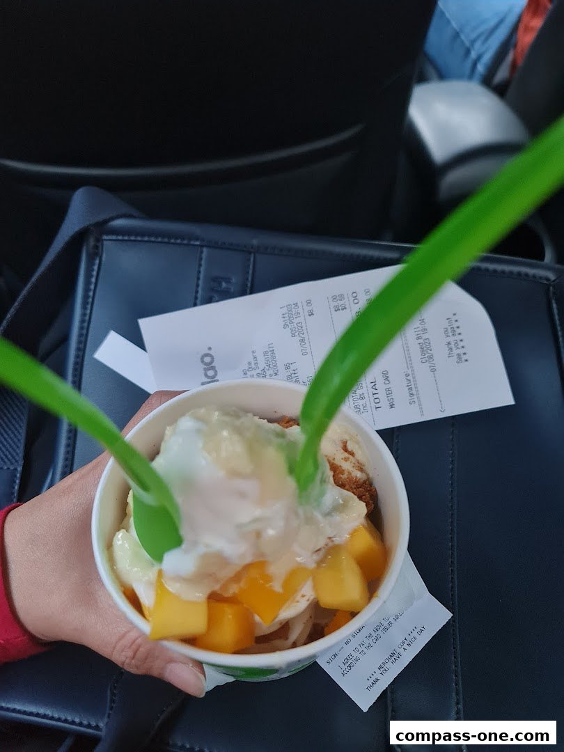 A hand holds a cup of frozen yogurt with mango and toppings, with a receipt in the background.
