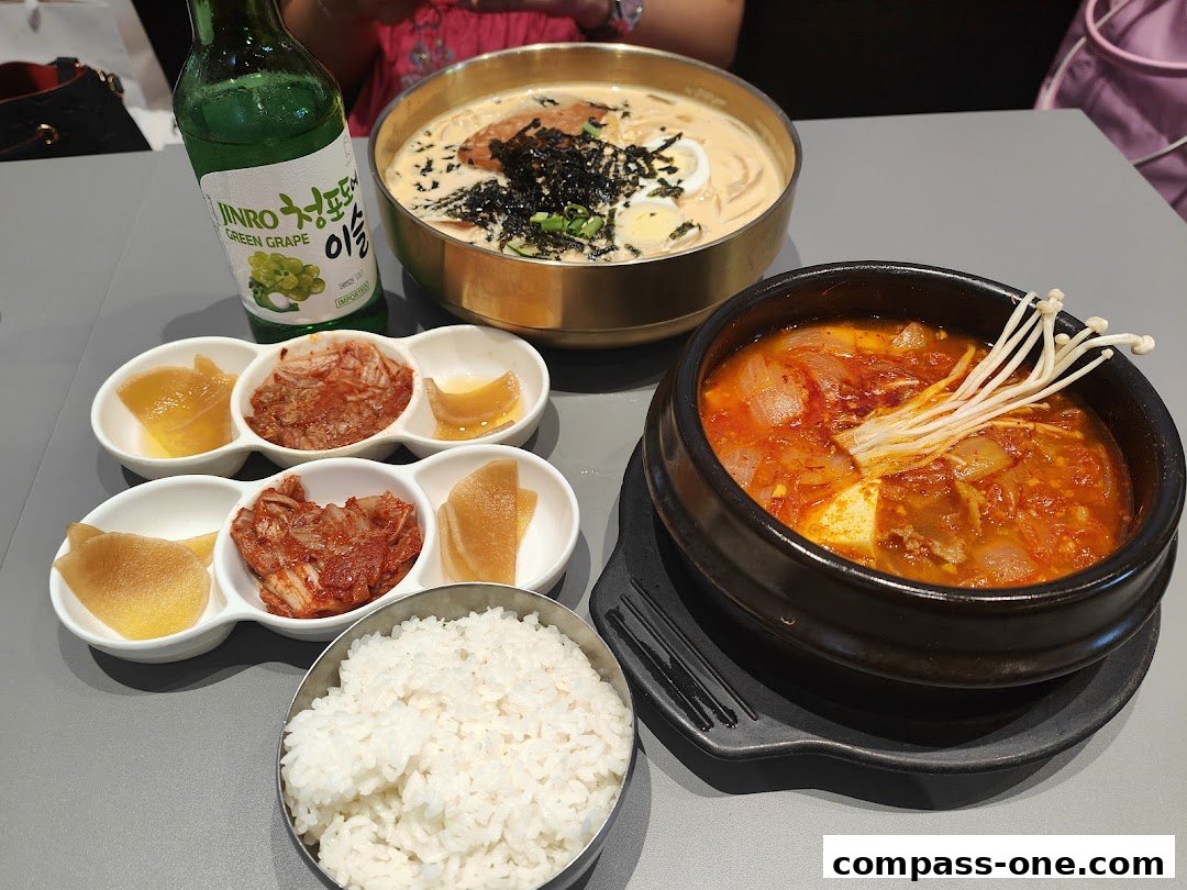 A table setting with Korean dishes, including kimchi, rice, soup, and a bottle of soju.