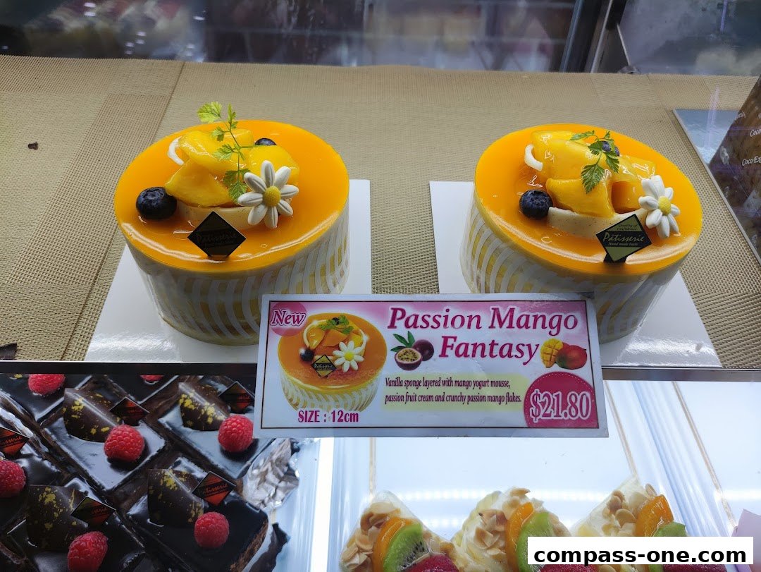 Two beautifully decorated cakes with mango and berries, displayed in a bakery case.