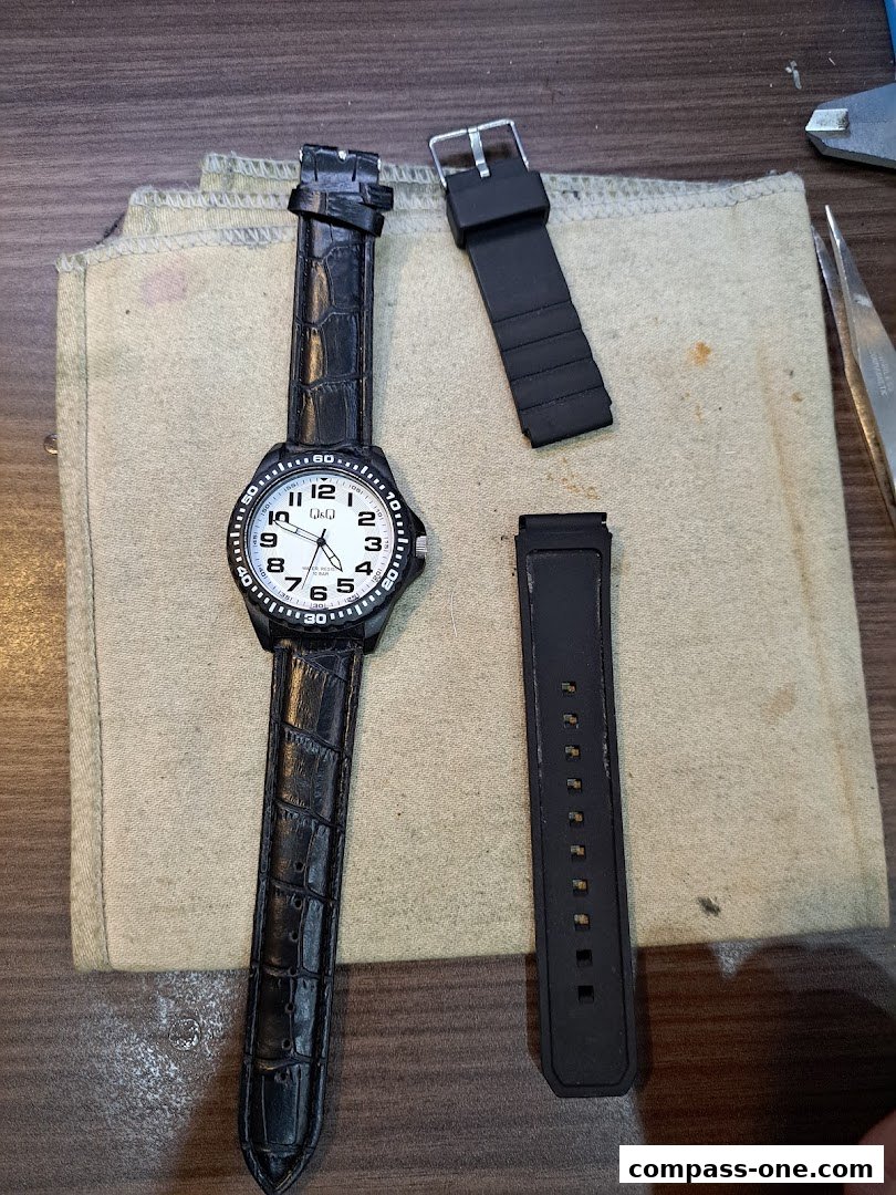 A watch with a black leather strap and a spare black rubber strap are laid out on a cloth.