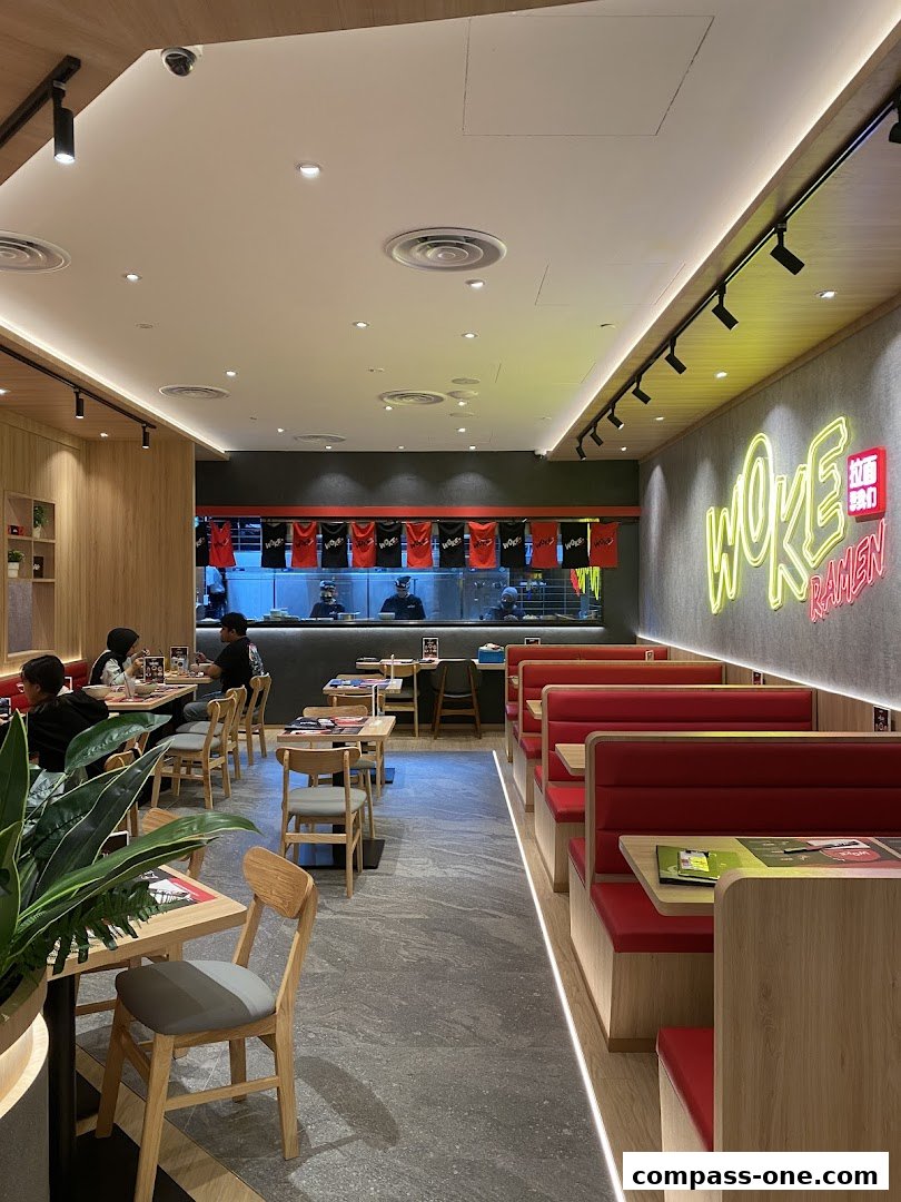 Interior view of WOKE Ramen restaurant with seating, neon sign, and kitchen view.