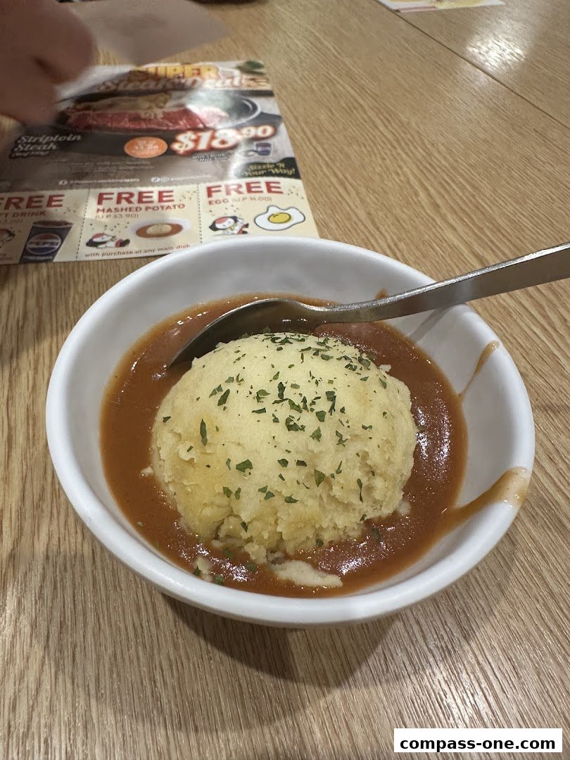 A bowl of mashed potatoes with gravy, served with a menu in the background.