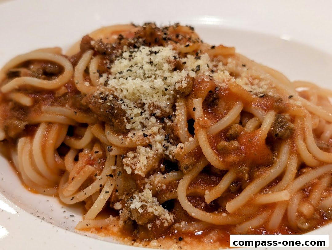 A close-up shot of spaghetti bolognese topped with grated cheese and herbs.
