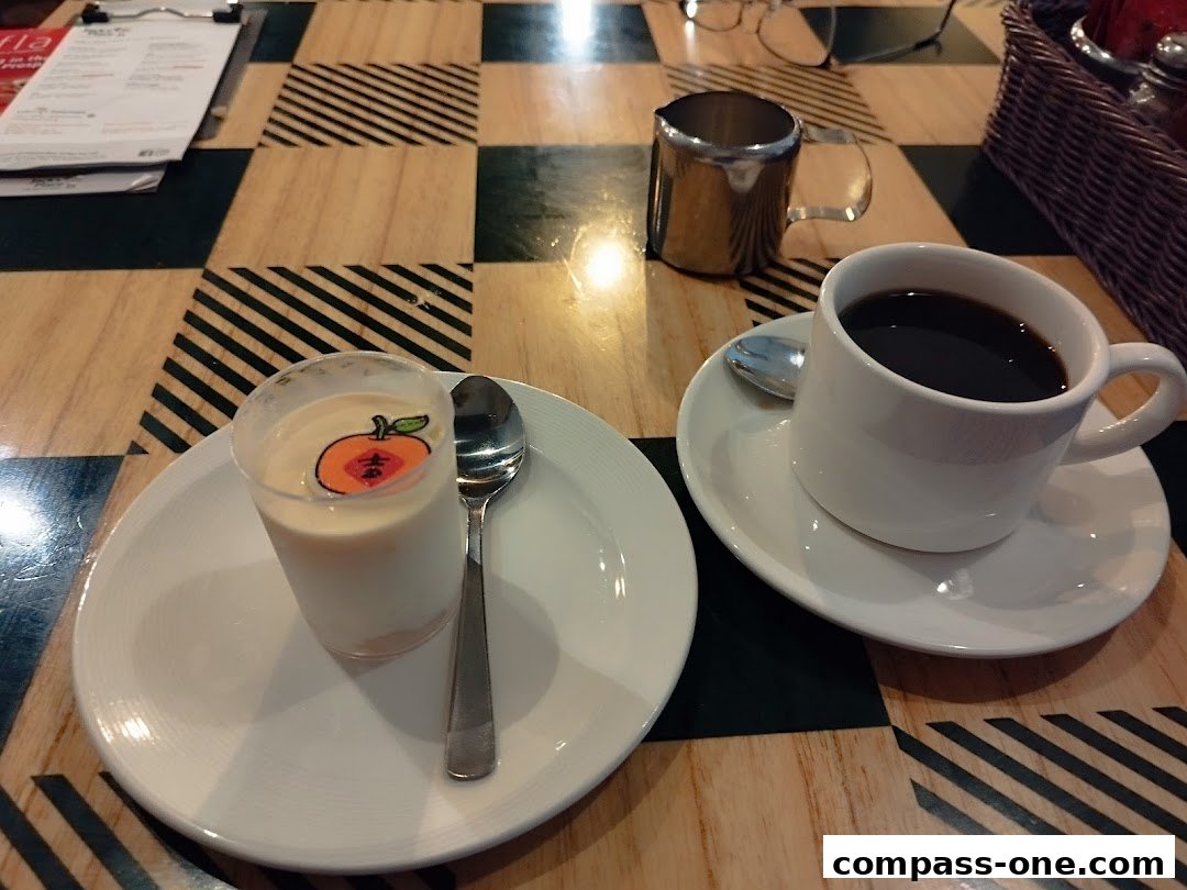 A cup of coffee and a dessert with a decorative orange slice on a checkered table.