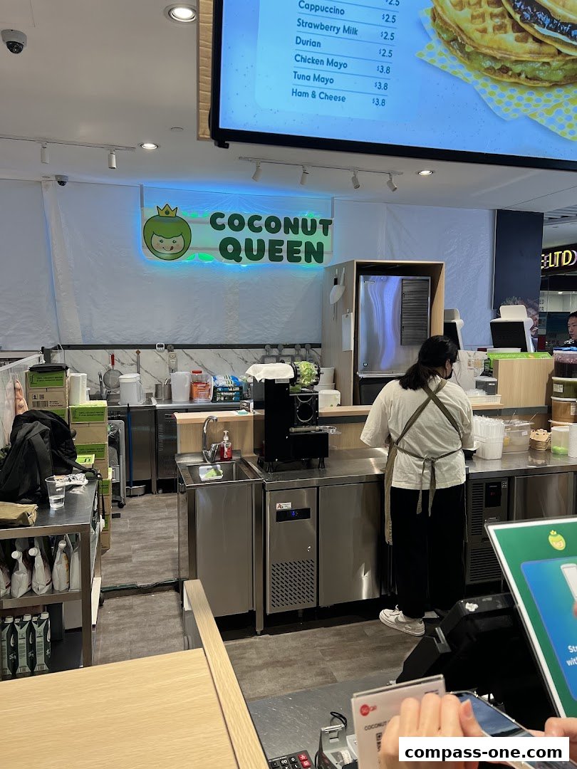 A brightly lit food stall with a prominent "Coconut Queen" sign and a menu displayed above.