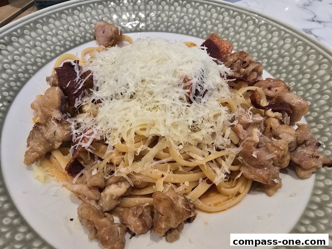 A plate of linguine pasta topped with shredded cheese and pieces of meat.