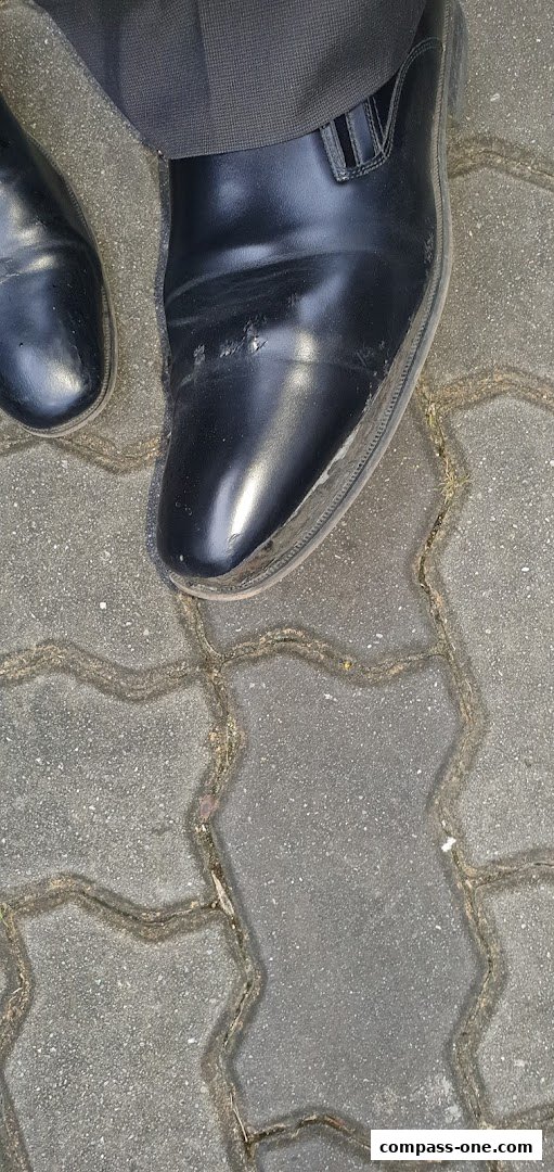 A close-up view of a person wearing black formal shoes on a paved walkway.