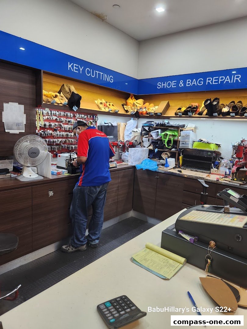 A Mister Minit employee performs key cutting services with shoe and bag repair displayed.