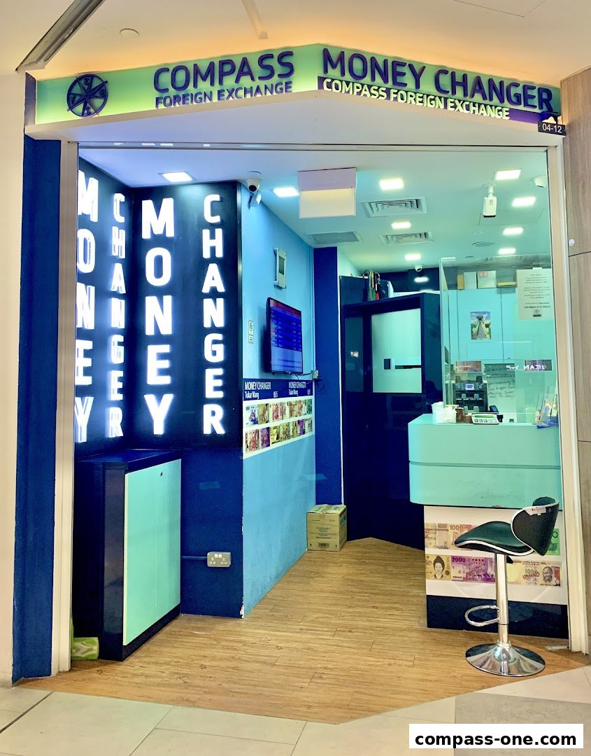 The entrance of Compass Money Changer, a foreign exchange service with bright signage and a clean interior.