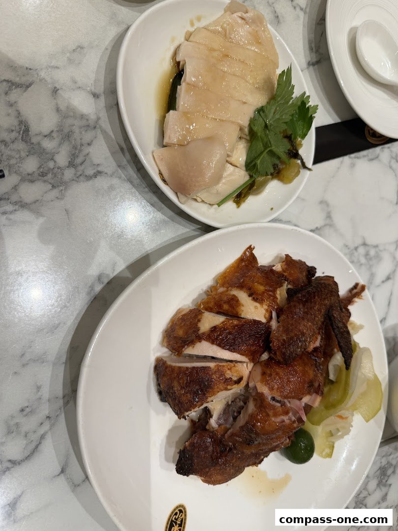 Two plates of chicken, one steamed and one roasted, served with garnishes.