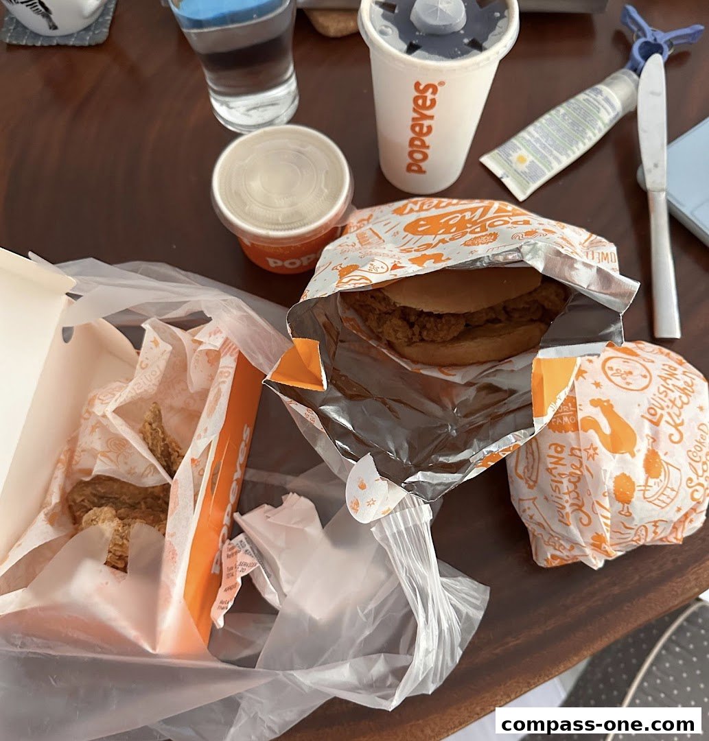 A table laden with Popeyes fried chicken, a sandwich, and drinks.