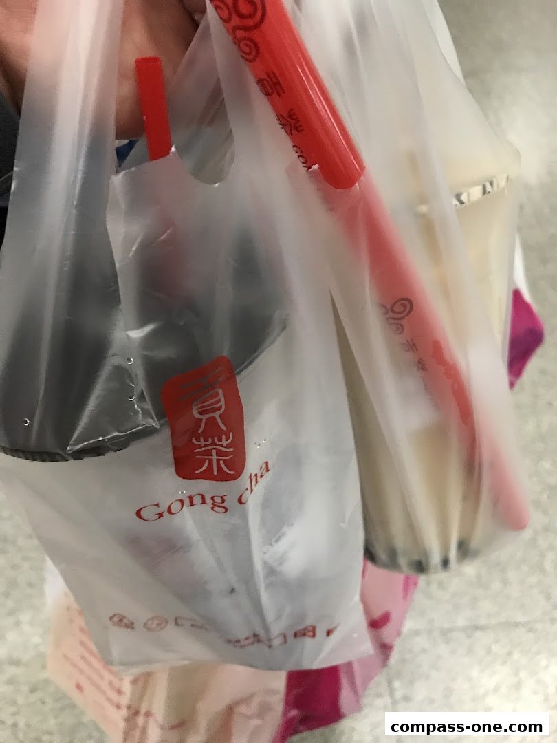 A person holding two Gong Cha branded plastic bags with drinks and straws.