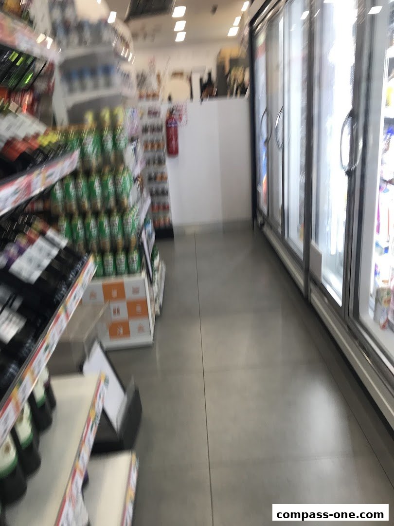 Aisle view of a 7-Eleven store with shelves of drinks and refrigerators.