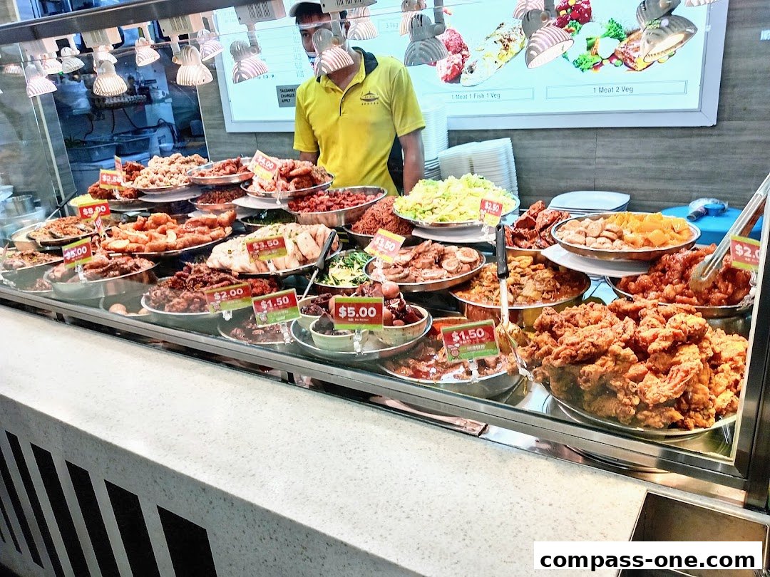 A display of various cooked dishes and fried chicken at a food stall.