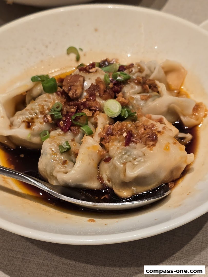 A close-up shot of delicious dumplings in a savory sauce, garnished with scallions and crispy bits.