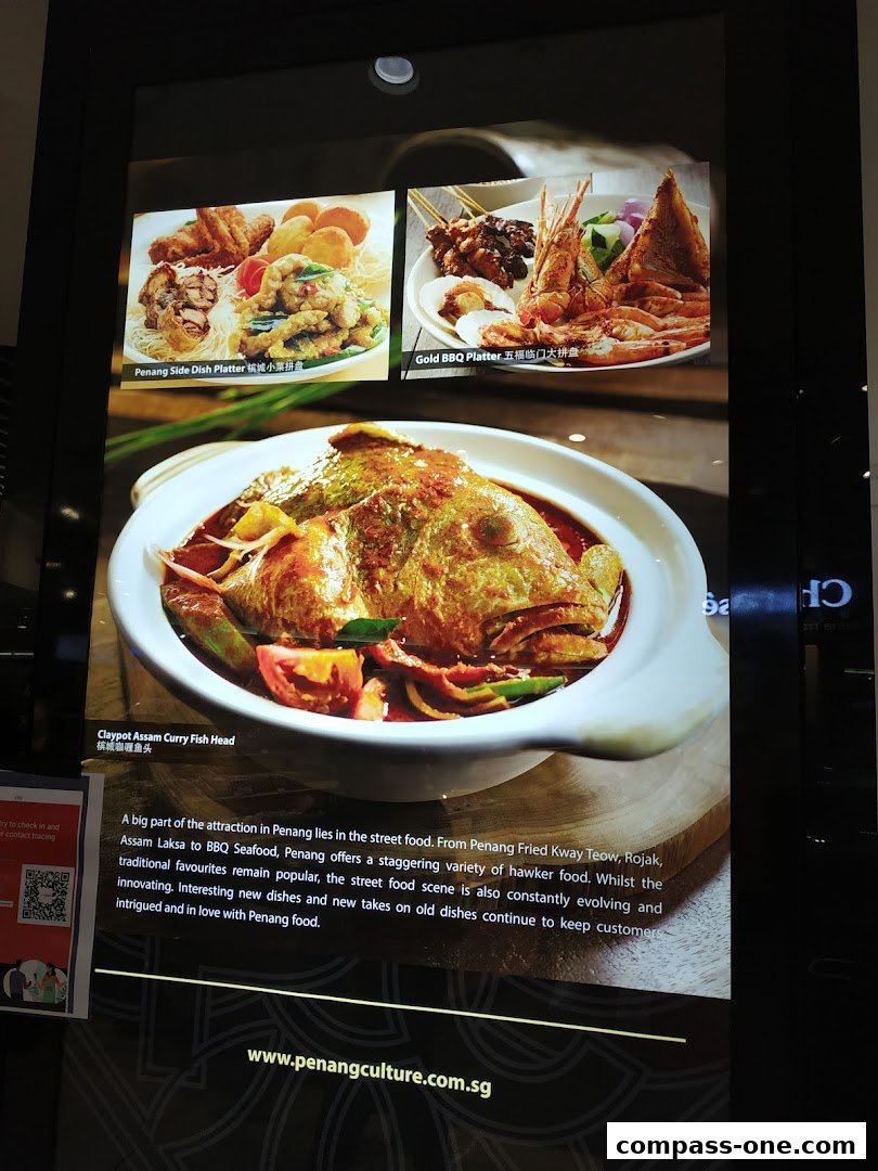 A display board showcasing three popular Penang dishes: a side dish platter, a BBQ platter, and a curry fish head.
