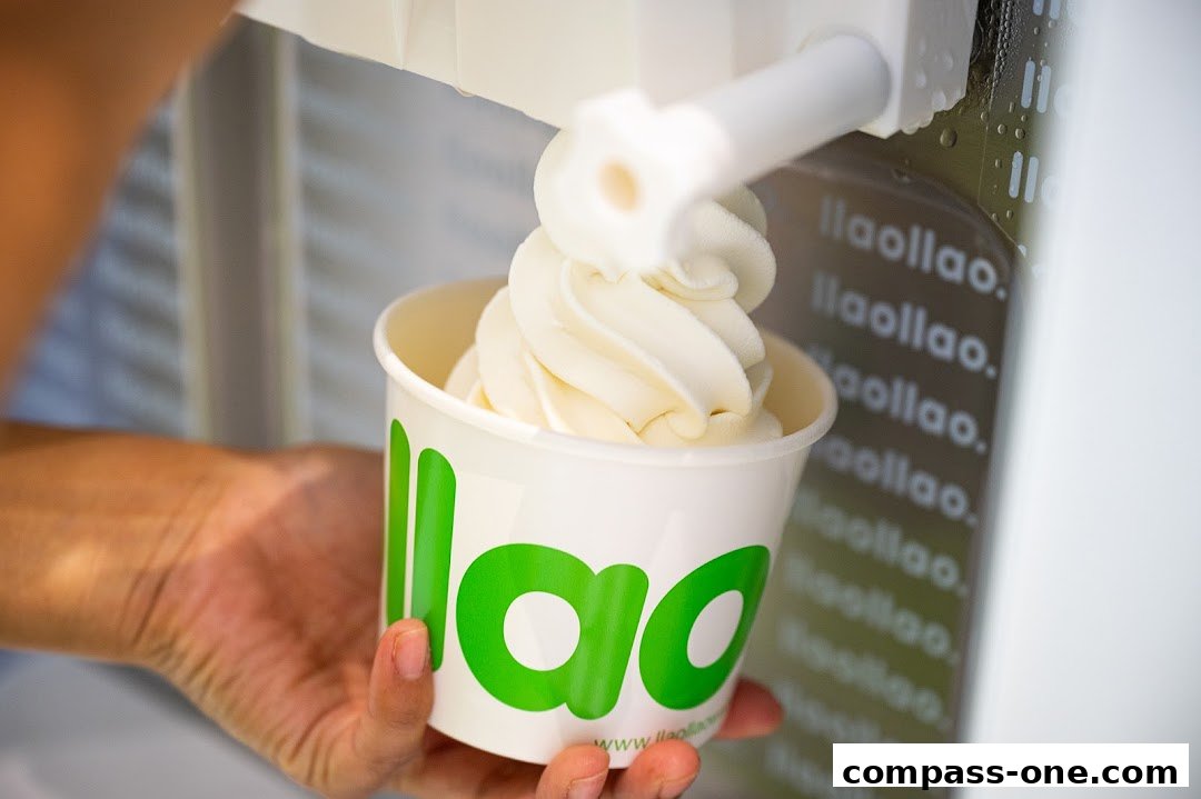 A hand holds a cup of frozen yogurt being dispensed from a machine.