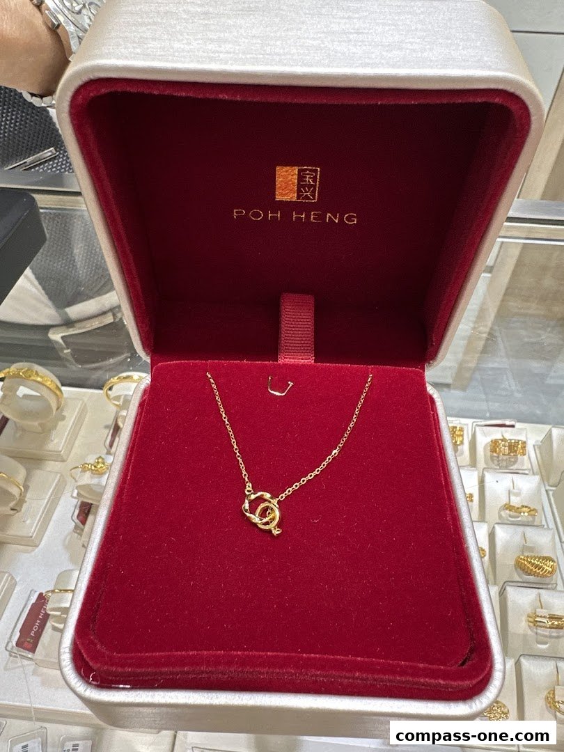 A gold necklace displayed in a Poh Heng Jewellery gift box, surrounded by other jewelry.