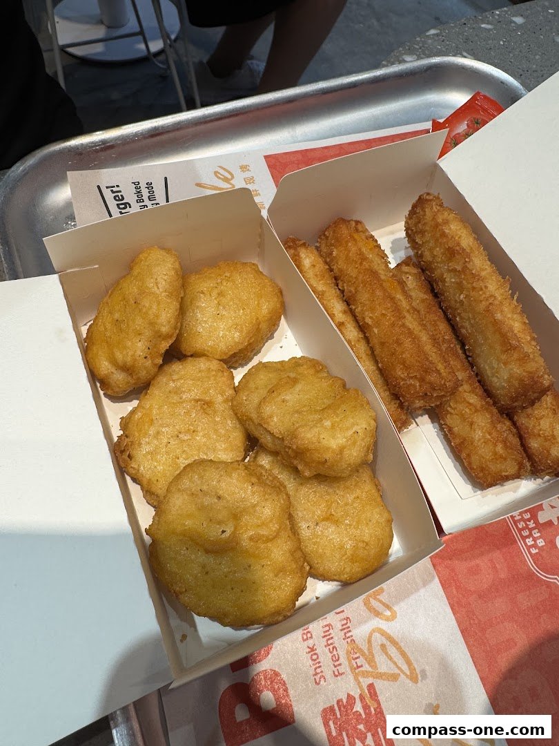 A close-up shot of chicken nuggets and fries served in white paper boxes on a metal tray.