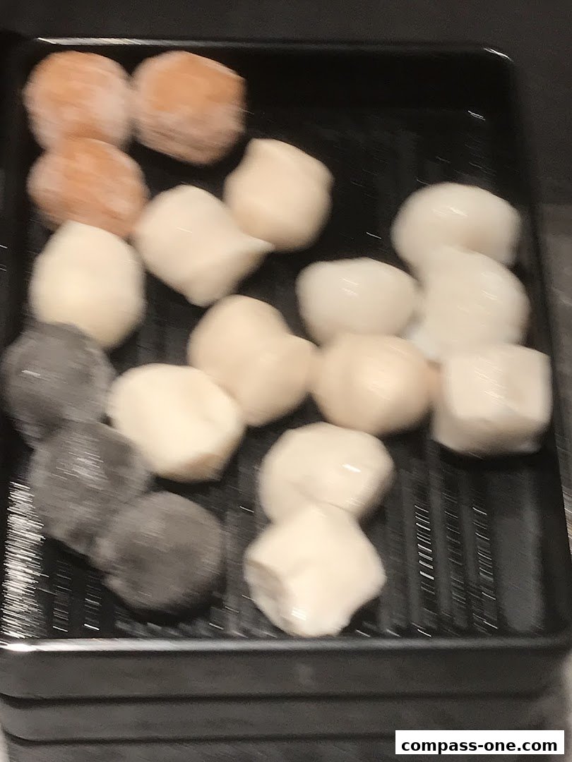 A black tray filled with various types of food balls, some appear frozen.