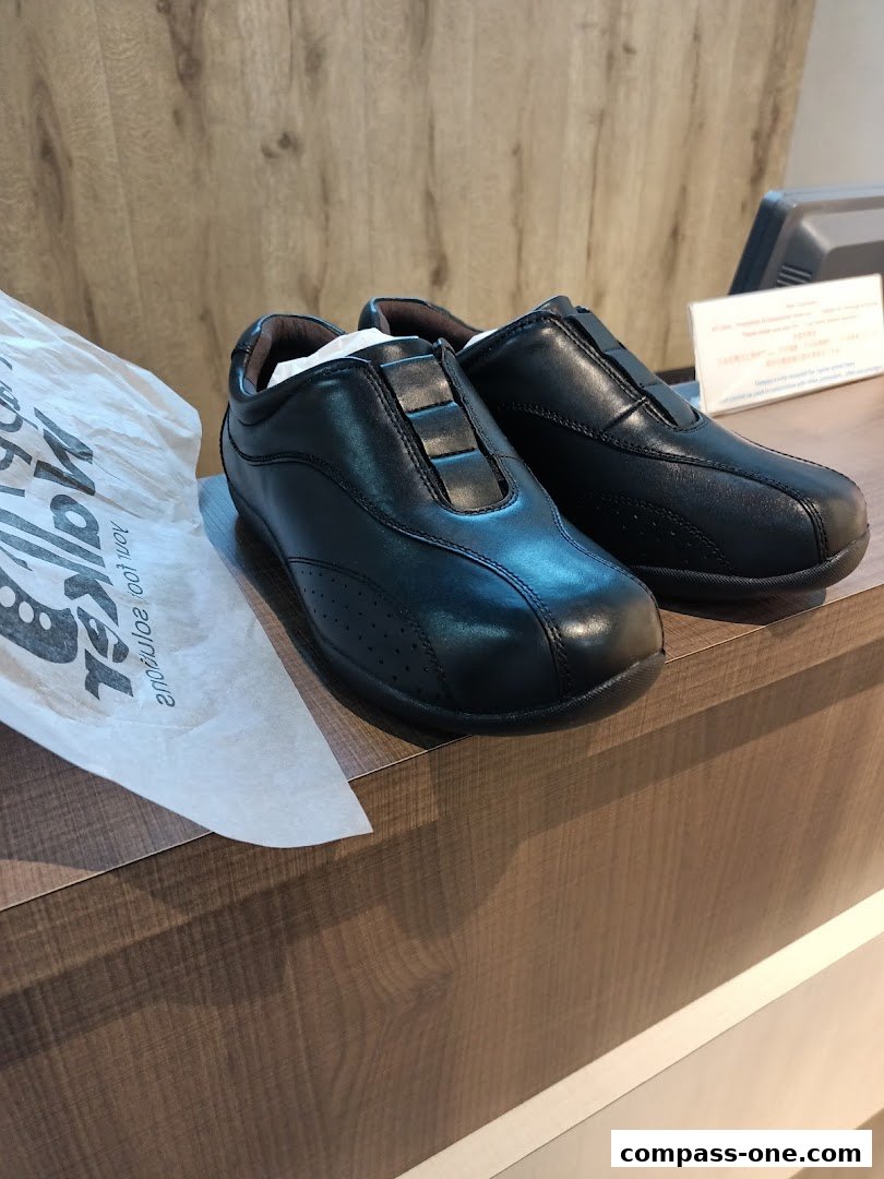 A pair of black leather slip-on shoes displayed on a wooden counter with a shopping bag.