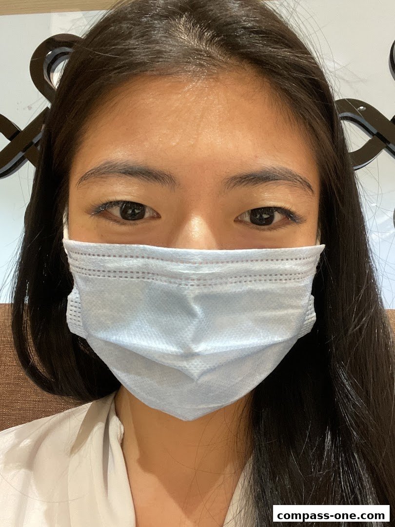 A close-up of a young woman wearing a light blue surgical mask.
