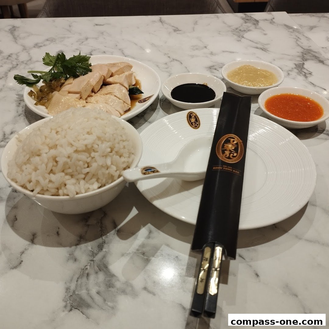 A plate of sliced chicken with rice, sauces, and chopsticks on a marble table.