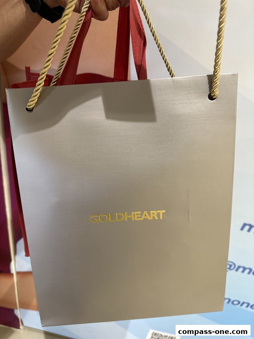 A person holds a grey shopping bag with the Goldheart logo in gold.