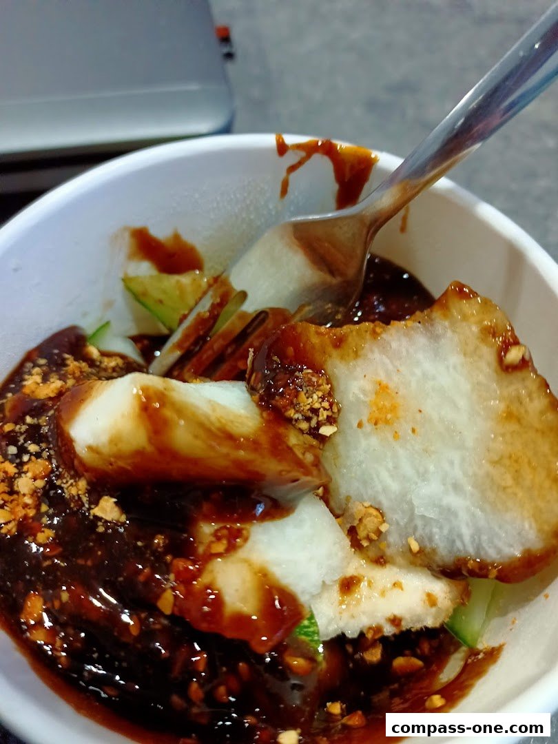 A close-up shot of a bowl of Laksa with a spoon, featuring noodles, broth, and toppings.