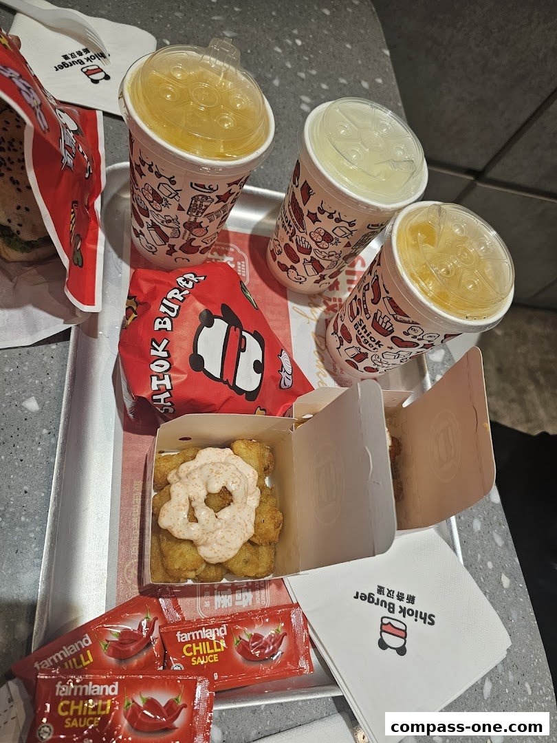 A tray of food from Shiok Burger, including burgers, drinks, and tater tots with sauce.