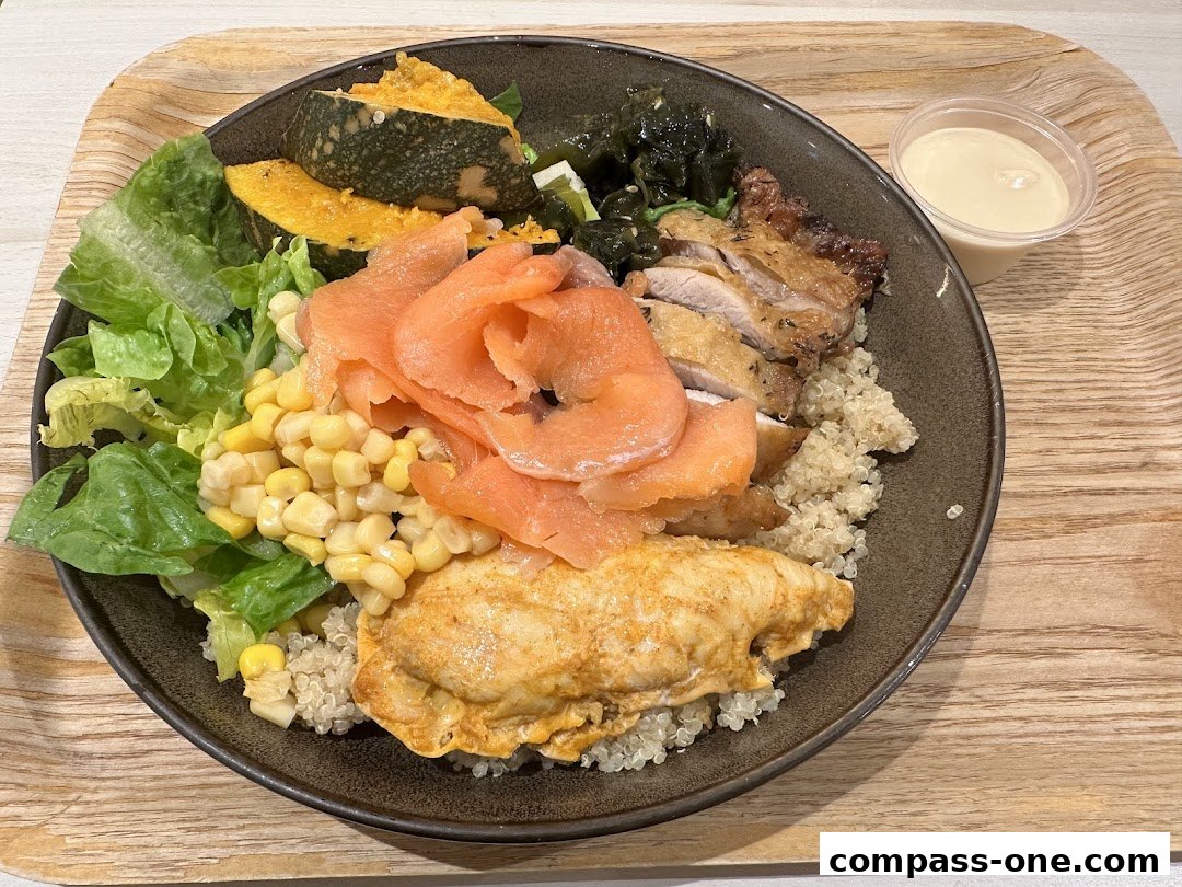 A healthy grain bowl with salmon, chicken, corn, pumpkin, and greens, served with a side of dressing.