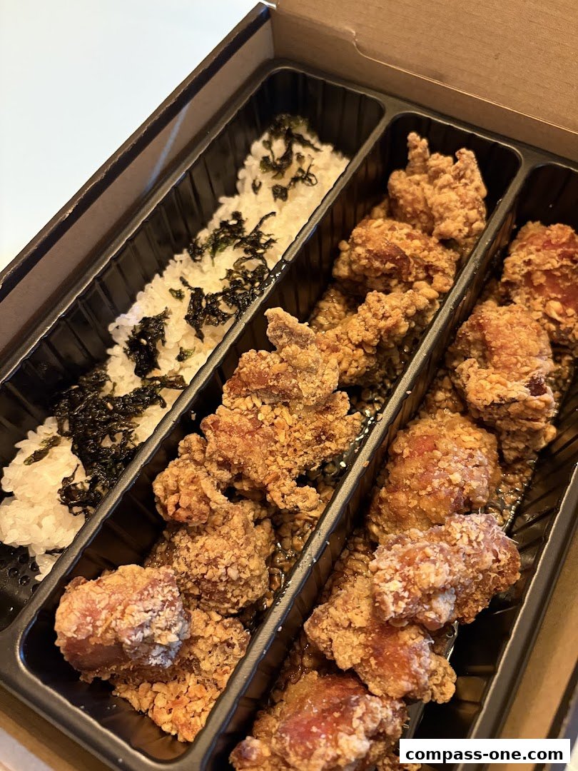 A takeaway box filled with crispy fried chicken pieces and rice with seaweed.