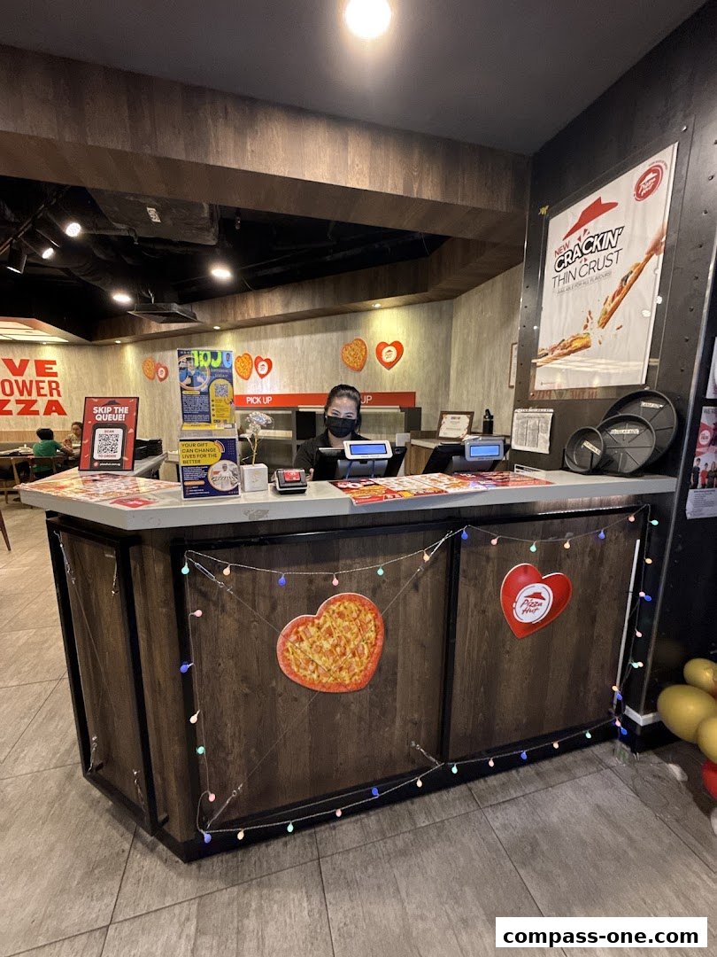 A Pizza Hut counter with a staff member wearing a mask, decorated with heart-shaped pizzas and lights.