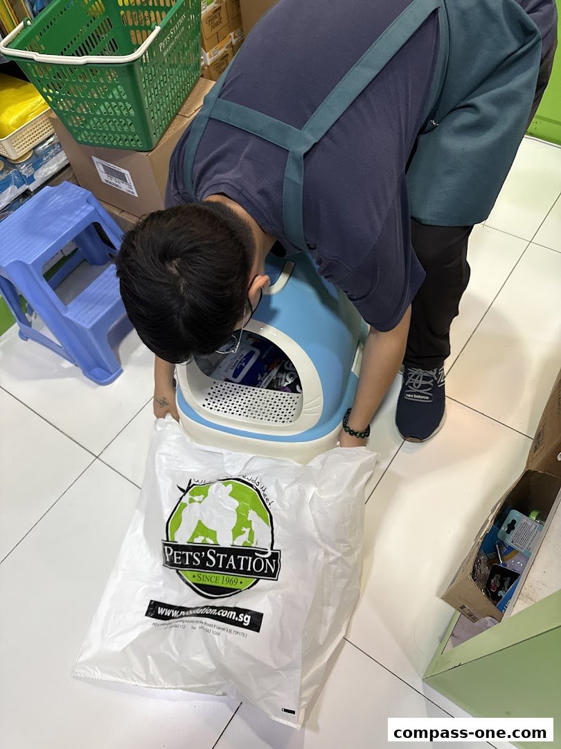A person in an apron is tending to a pet litter box with a shopping bag from Pets Station.